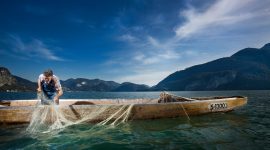 Mann mit Fischerboot und Fischernetz im See.